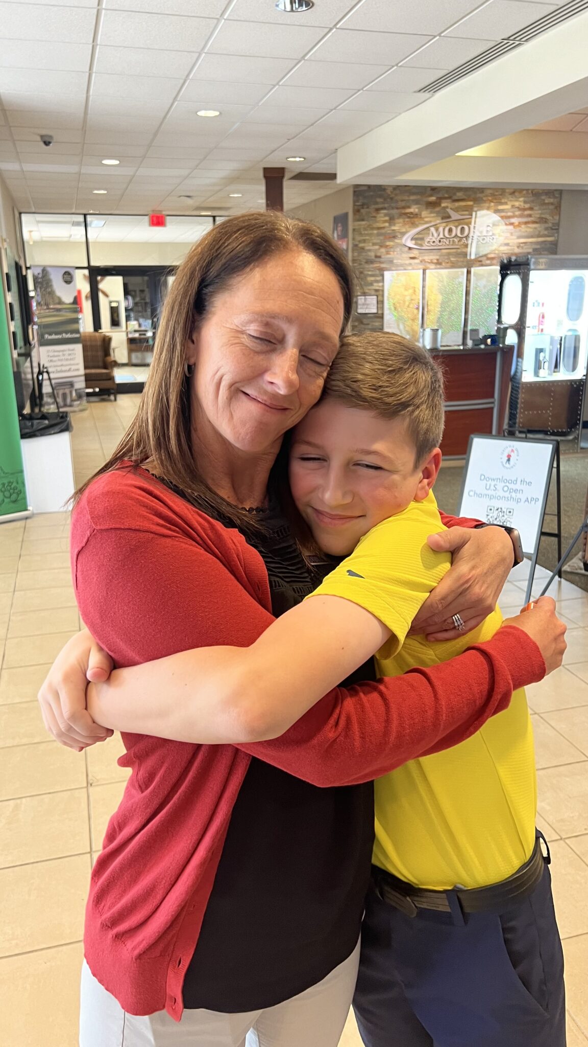 An adult and a young person sharing a long hug in an airport lobby.