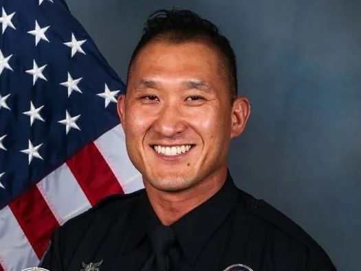 Detective Ryan So in Scottsdale Police Department uniform, photographed in front of a United States flag.