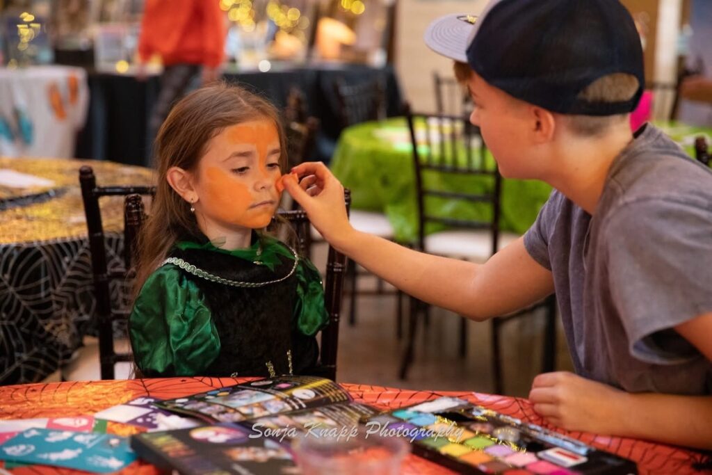 A youth volunteer face painting a young girl at a Children of Fallen Heroes event.