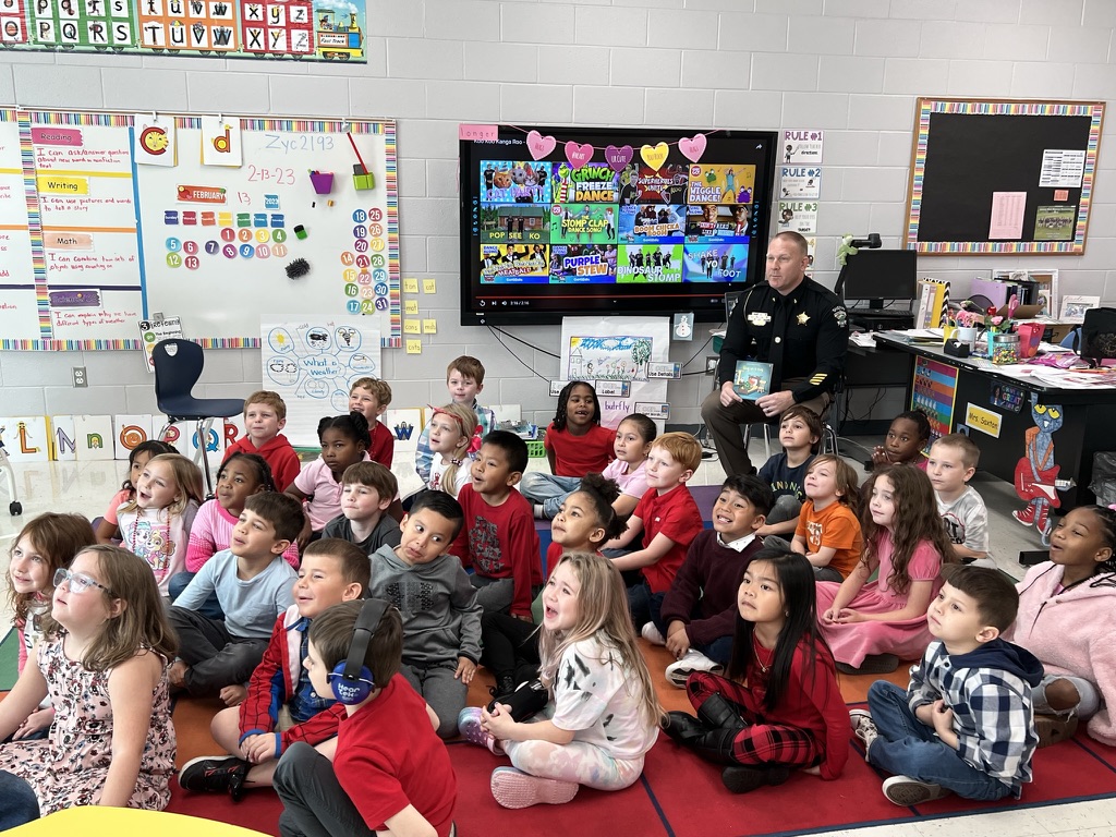 A sheriff's deputy reading a book to a classroom of young students.
