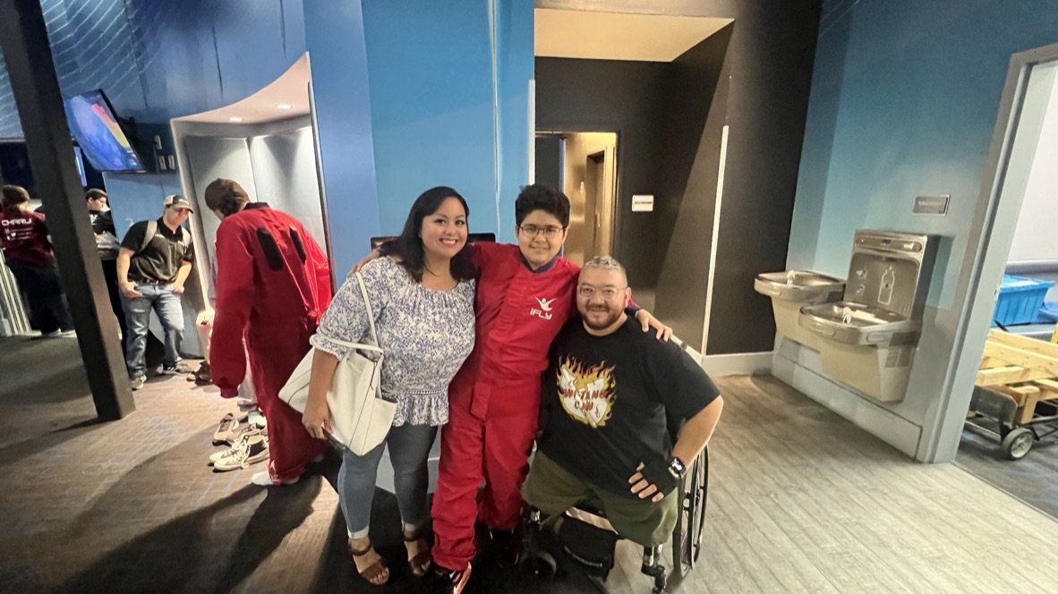 Adaptive veteran Craig Armstrong with his wife and son at iFLY San Antonio, his son wearing a red indoor skydiving flight suit.