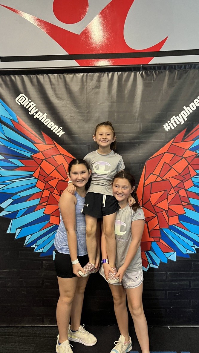 Detective Ryan So&rsquo;s three daughters together at iFLY Phoenix, the two older sisters holding their younger sister between them.