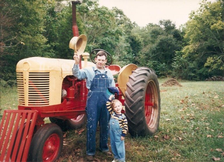 A farmer and a young child beside a vintage tractor in a field.